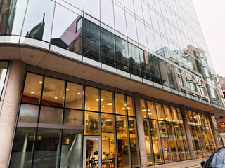 Naklejka premium Modern glass office building in Manchester, UK, with glass facade and warm The Flokk showroom interior lighting visible