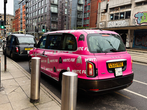 Pink LEVC TX taxi cab on a Manchester street with modern buildings and pedestrians in the city centre UK