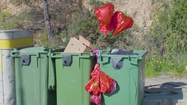 Deflated heart-shaped balloons blowing in the wind near a trash can