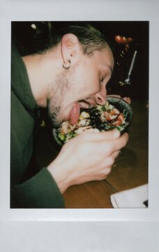 A man sticks out his tongue and dips his head into a plate of food