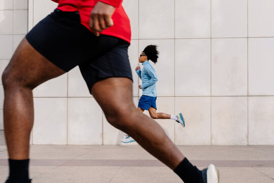 Sprinter running near a building with the legs of a mate in foreground