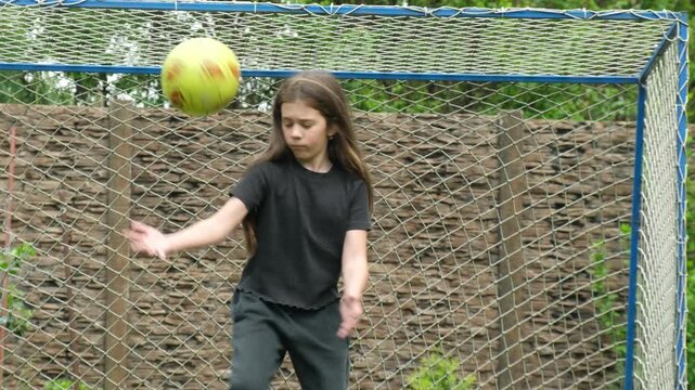 Determined young girl with long hair acting as a goalkeeper, trying to save a goal but misses the ball, showcasing a failed attempt during a backyard soccer game in slow motion