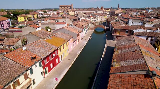Comacchio aerial 4k reverse flight over canal with pigeons in Italy. Yellow and red houses of Little Venice in Emilia Romagna. Cinematic pull back along water canal scenery
