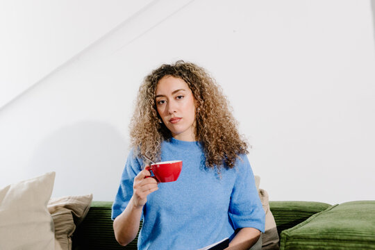 Freelance woman sitting on a living room sofa, clutching a coffee cup