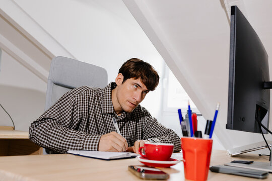 Self-employed professional at a home desk, writing notes in a notebook