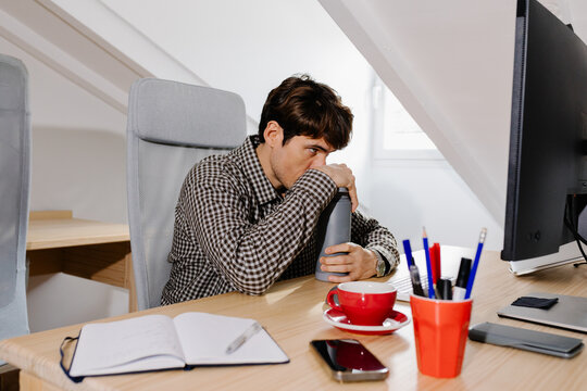 Freelancer staring at his computer with tired gaze at his home office