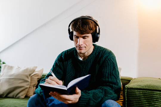 Freelance man jotting notes for his schedule while listening to music