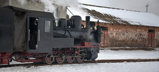 A narrow-gauge railway.A steam locomotive at a railway station. A winter, tourist, retro voyage. A steam locomotive in all its glory. Rolling stock at a railway station. © Valerii