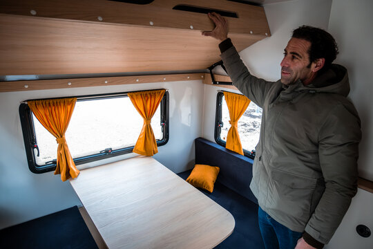 Man reaching for overhead cupboard in a tiny home camper van interior, illustrating efficient storage and space-saving design for van life