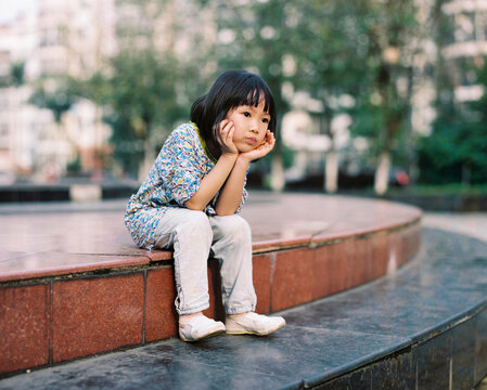 Chinese child rests his head in his hands, deep in thought, on steps 