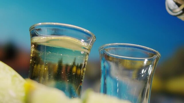 Mexican Tequila Mezcal pouring with lime and salt on a stone table. Strong vodka rum alcoholic drink is poured from a bottle into a shots.
