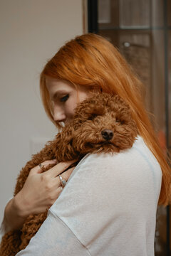 Woman holds a poodle close in a warm indoor setting