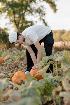 A teenage boy at a pumpkin patch, picking a pumpkin for Halloween.