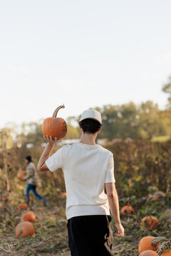 A teenage boy at a pumpkin patch, picking a pumpkin for Halloween.