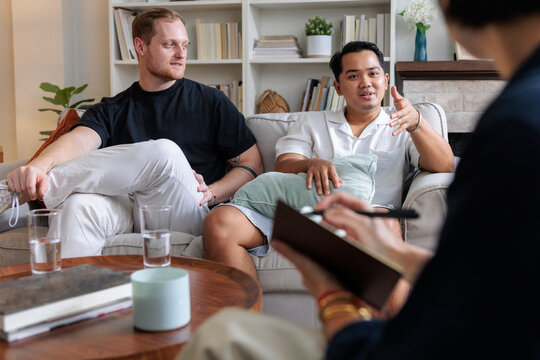 Couple in therapy session, therapist taking notes.