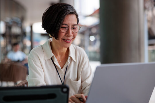 Woman smiles while working on laptop at outdoor cafe.
