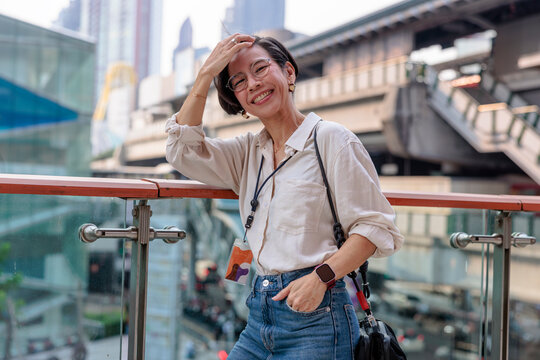 Smiling woman in city setting, leaning on railing.