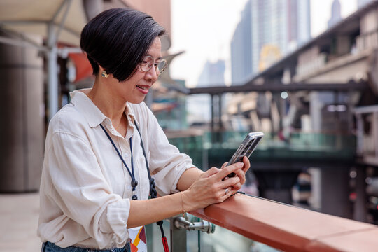 Woman uses phone on city balcony, buildings in background.