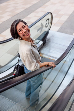 Smiling woman rides escalator, looking up at the camera.