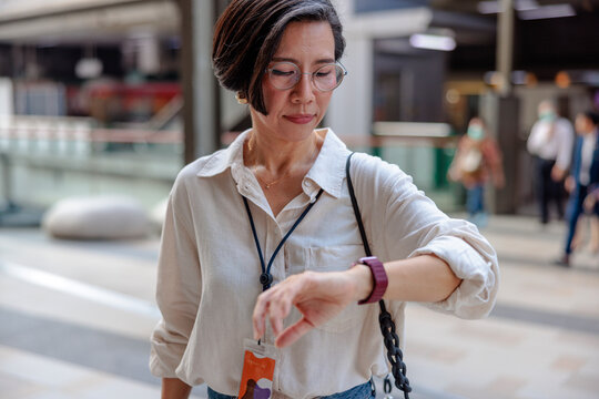 Woman checks watch in public space, people in background.