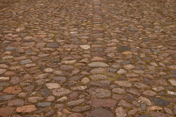 Weathered Cobblestone Street Surface Showing Uneven Rounded Stones, Warm Brown Tones, Aged Mortar, Subtle Moss Patches, Lowangle Closeup Emphasizing Texture And Pattern, Historic Urban