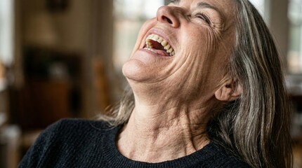 Joyful mature woman with gray hair laughing heartily, head tilted back in a moment of pure happiness indoors