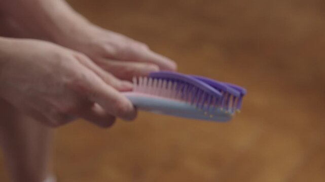 Close-up of person cleaning pink bristle hairbrush with purple comb for improved scalp health and personal hygiene, maintaining hair care tools for daily grooming routines. Shooting in slow motion.