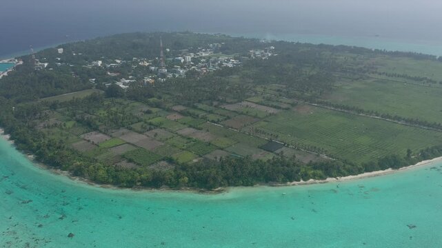 Wide aerial panoramic view of entire Thoddoo island revealing extensive agricultural farming fields, the local village, lush palm forests, and surrounding turquoise coral reefs.
