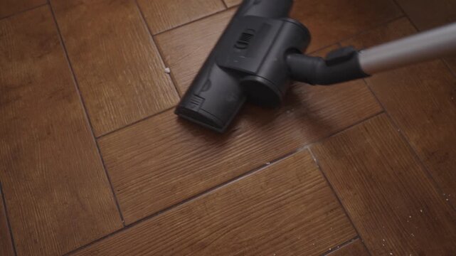 Closeup top view of vacuum cleaner attachment head sucking dust and debris from under cabinet, providing deep cleaning and maintaining domestic hygiene in modern home environment.