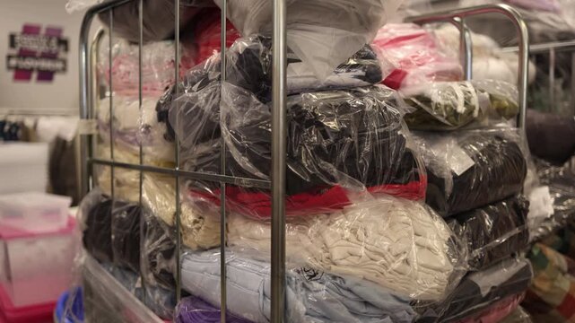 Stacks of unsold clothing packed in plastic bags fill metal carts awaiting disposal highlighting excess production waste and the growing issue of discarded garments in the retail industry