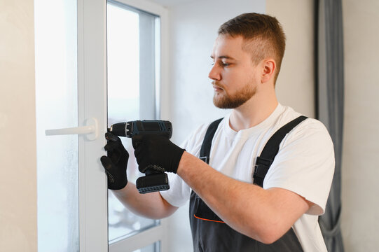 Man worker fixing window handle with power drill
