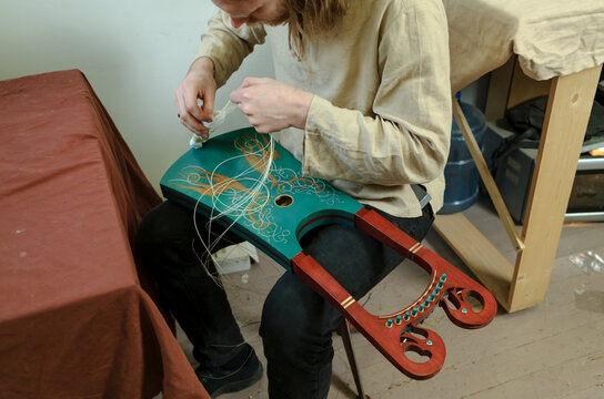 A luthier attaches strings to an instrument.