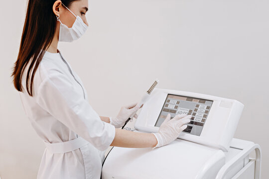 Medical technician operating cosmetic laser machine in clinic wearing mask and gloves