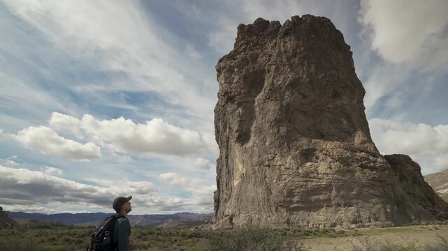 Hiker with a backpack looking at a massive volcanic rock formation named as Piedra Parada in a desert valley of Patagonia Argentina