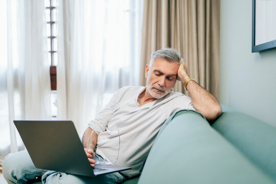 Tired man falling asleep on sofa with laptop