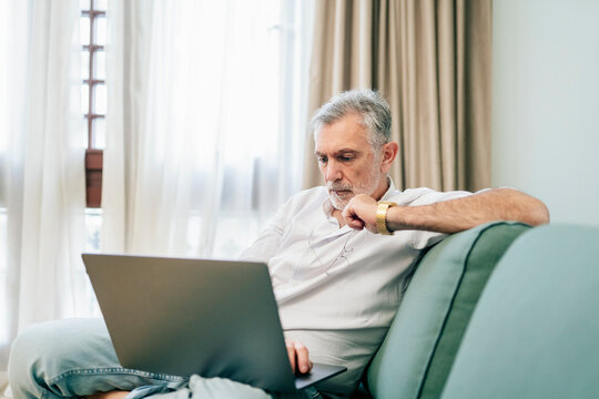 Senior man working remotely on laptop in hotel room