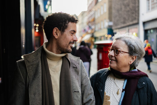 Adult son and senior mother smiling walking on city street