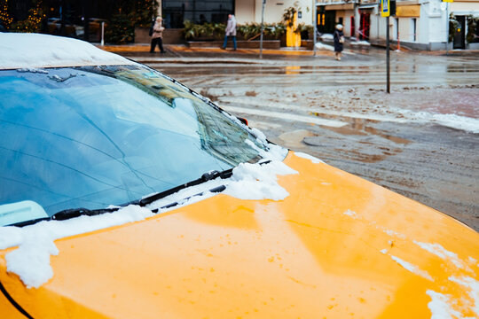 Snow covers yellow taxi on wet city street