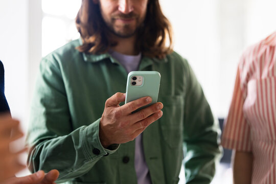 Man With Green Jacket Using Smartphone Among Friends