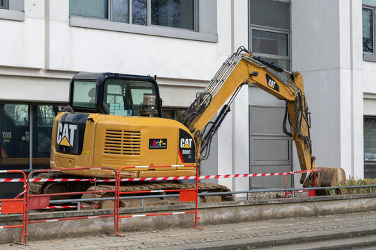 Nancy, France - February 28th 2026 : View on a small yellow crawler excavator CAT 308E2 CR for earthworks on a construction site with the facade of a modern building in the background.
