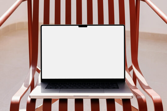 Laptop with white blank screen on red chair outdoors