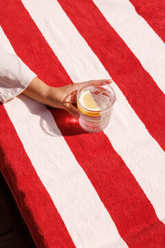 Hand holding glass of lemon water on striped towel