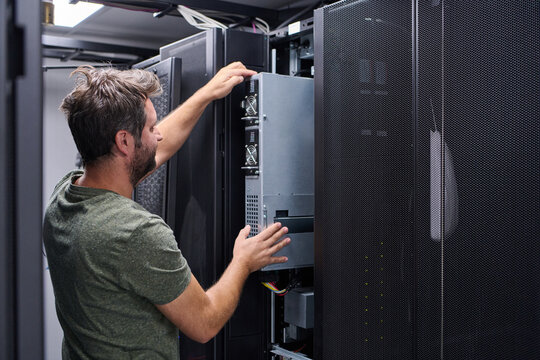 IT technician installing server hardware in a data center rack performing maintenance and configuration