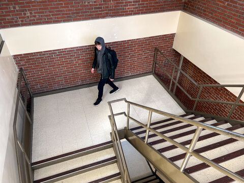 Teen with backpack walks down stairwell in a school building