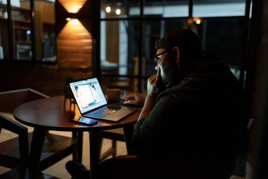 Side View Of Designer Working On Laptop At Night In Modern Interior