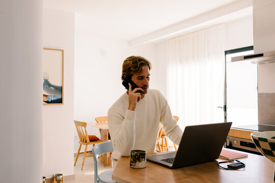 Man multitasking while answering a phone call and using a laptop
