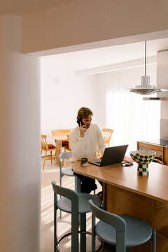Young man multitasking with laptop and phone in modern living room