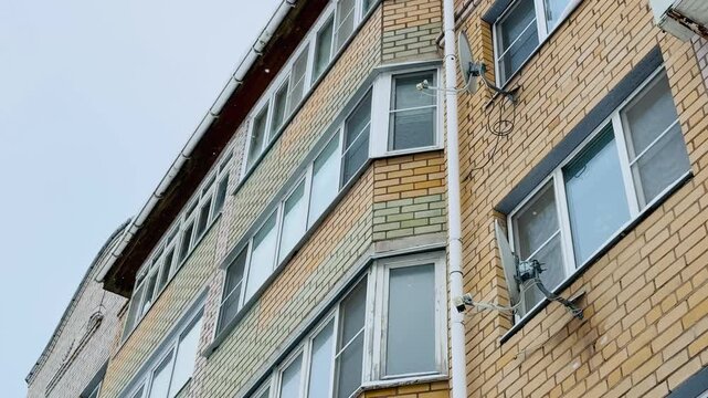 Cluster Satellite Dishes On Yellow Brick Facade With Tangled Cables And Rusted Mounts, White Window Frames And Angled Balconies, Corner Perspective Of Multi Storey Residential Building, DIY.