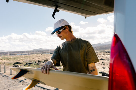 Young surfer pulling his surfboard from the open trunk of a van