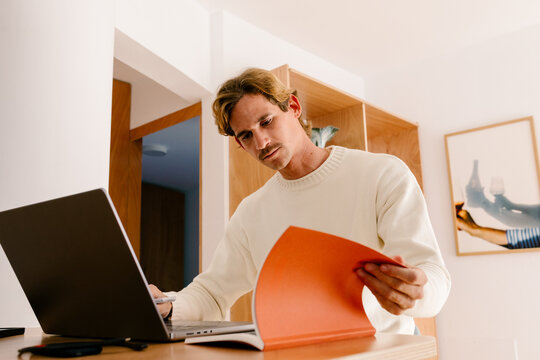 Man working on a computer referencing a book in a contemporary home